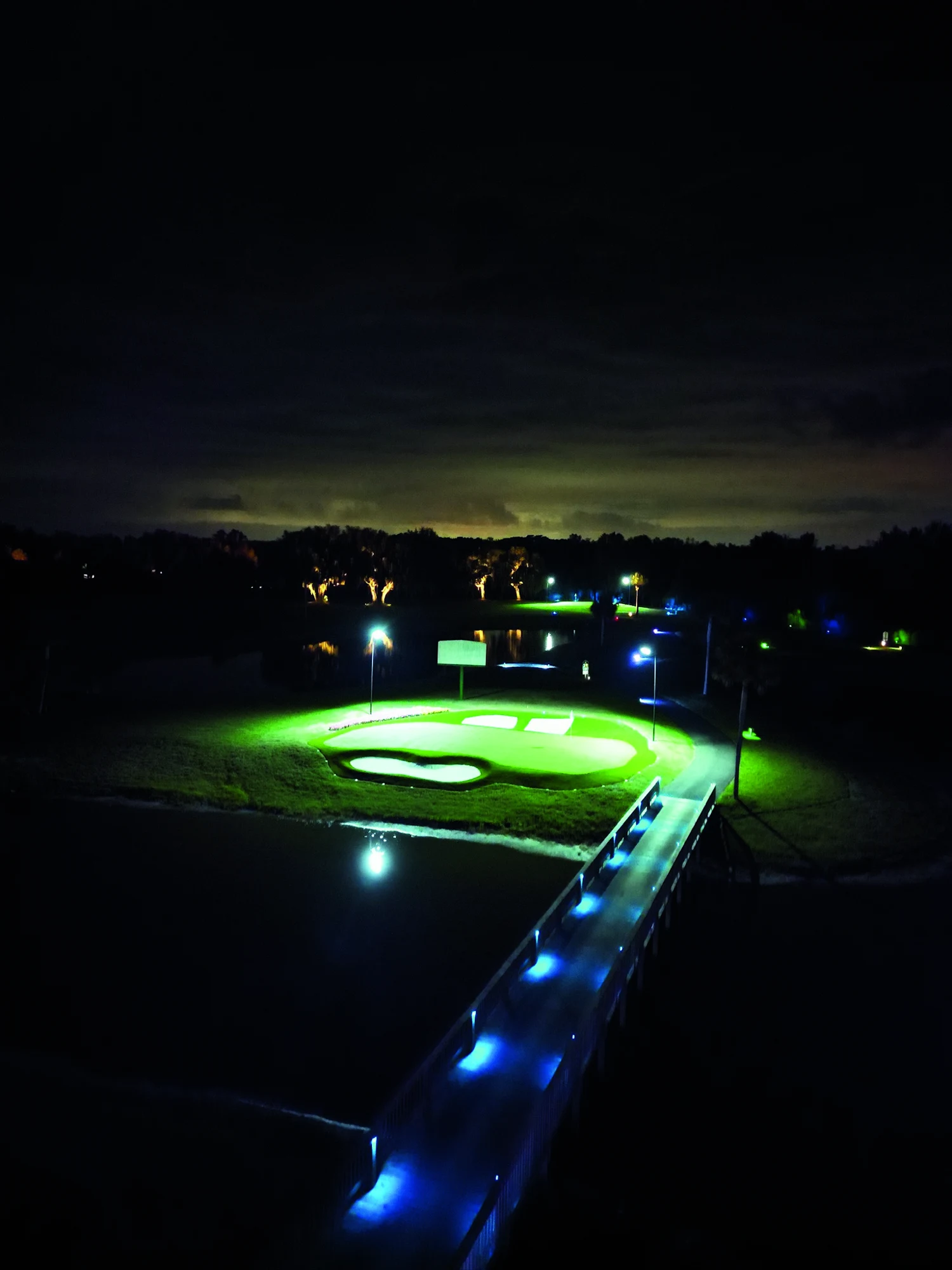 ZenWoods island green illuminated at night, with a bridge crossing the water